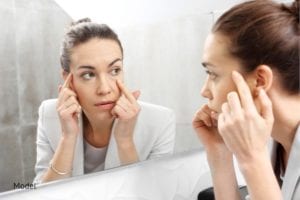Woman looking in the mirror considering how to make her eyes look more youthful